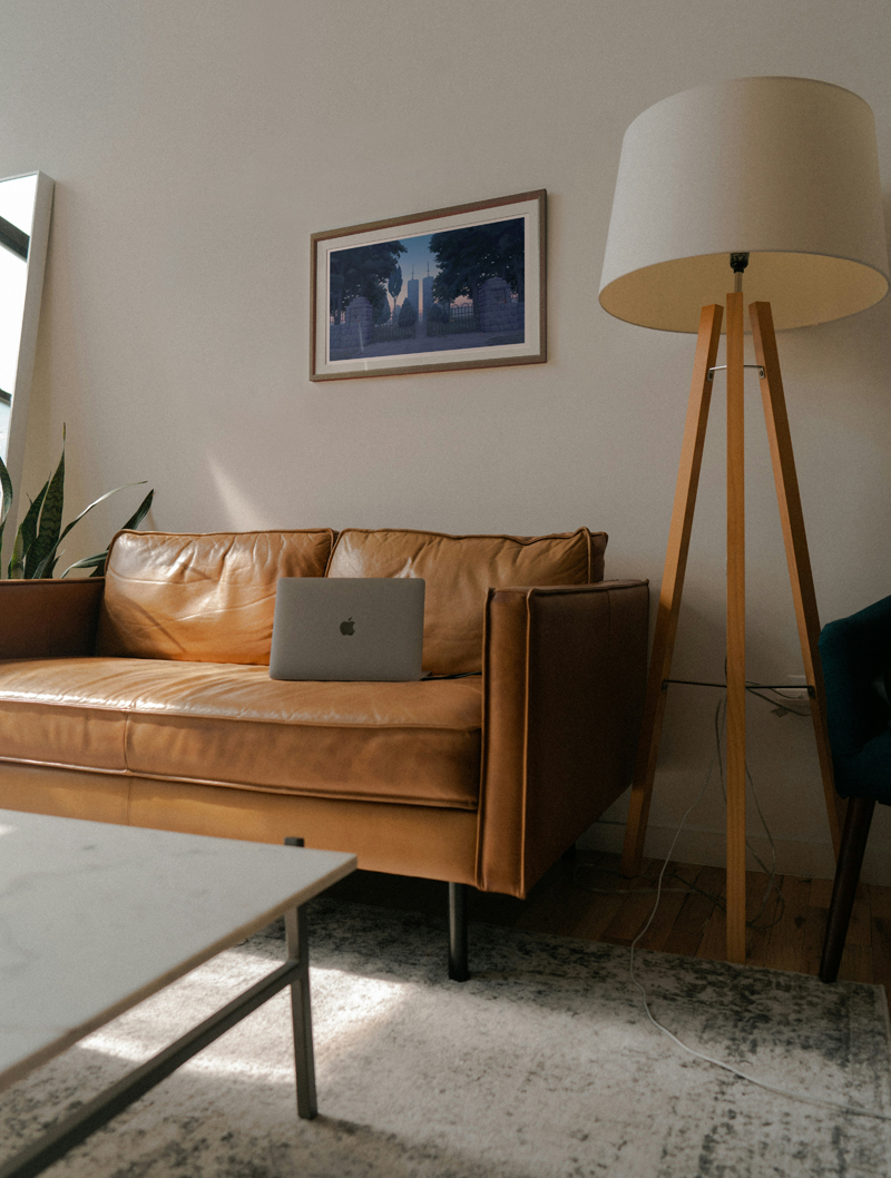 A photo of a living room. There is a couch with a laptop, a lamp next to it, and a framed print above it.