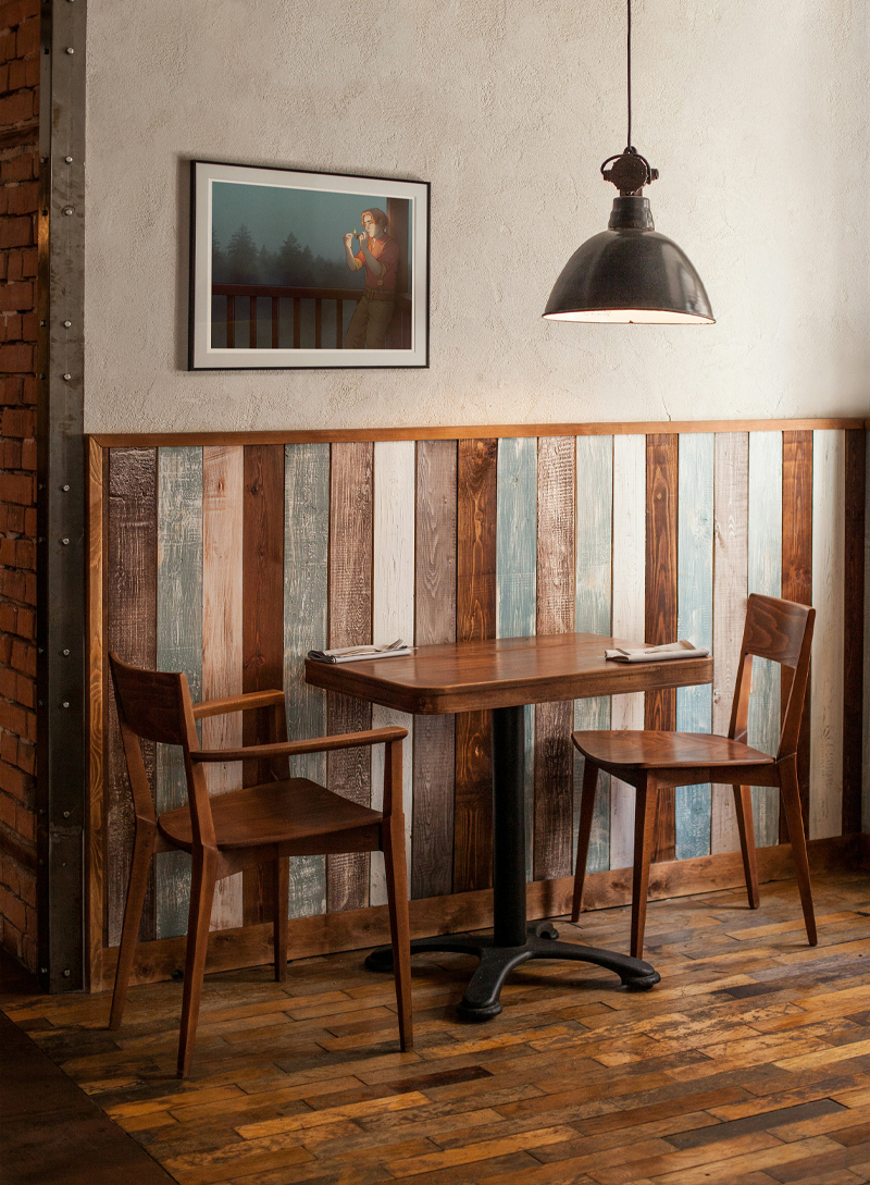 A photo from a cafe. It shows a coffee table with two chairs, a framed print, and a lamp above it. It is all kept in rustic style.